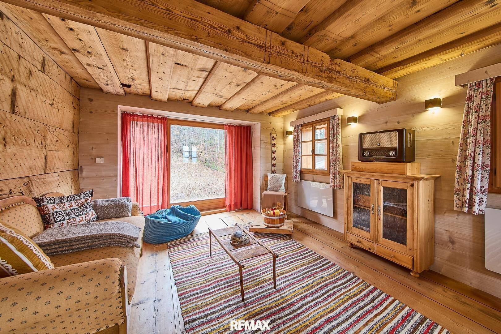 Gemütliches Wohnzimmer im alpinen Stil mit Holzbalkendecke, Holzboden und großem Fenster zum Garten.