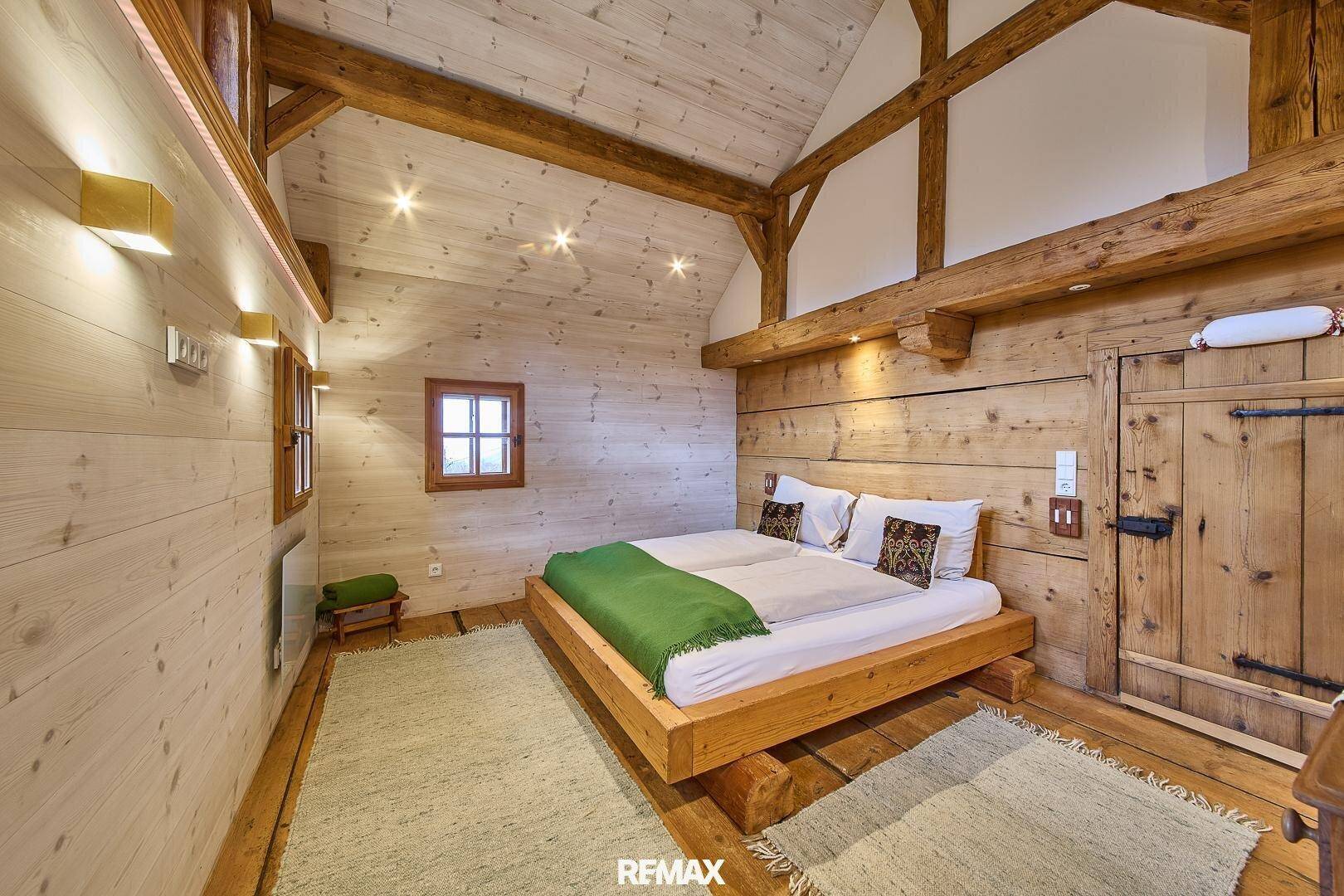 Schlafzimmer im Dachgeschoss mit Holzbalken, Holzwänden und einem großen Doppelbett.
