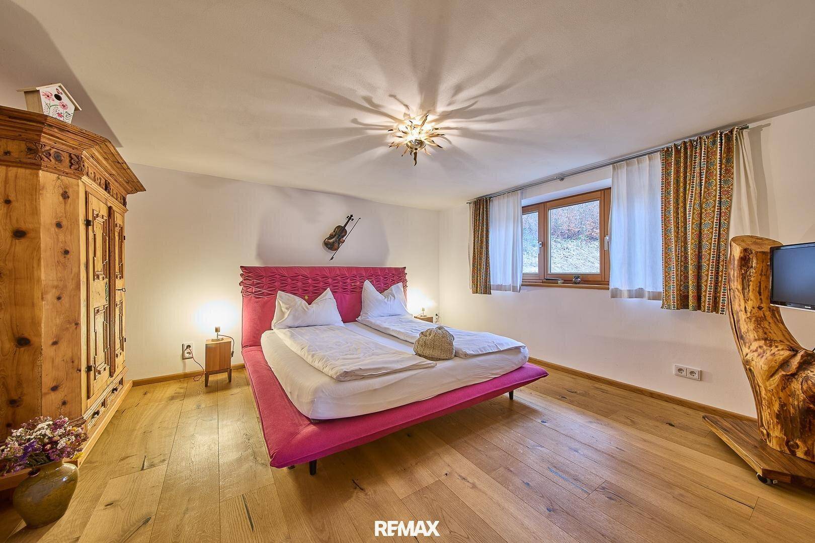 Geräumiges Schlafzimmer mit Holzboden, weiß gestrichenen Wänden und einem auffälligen pinken Bett.