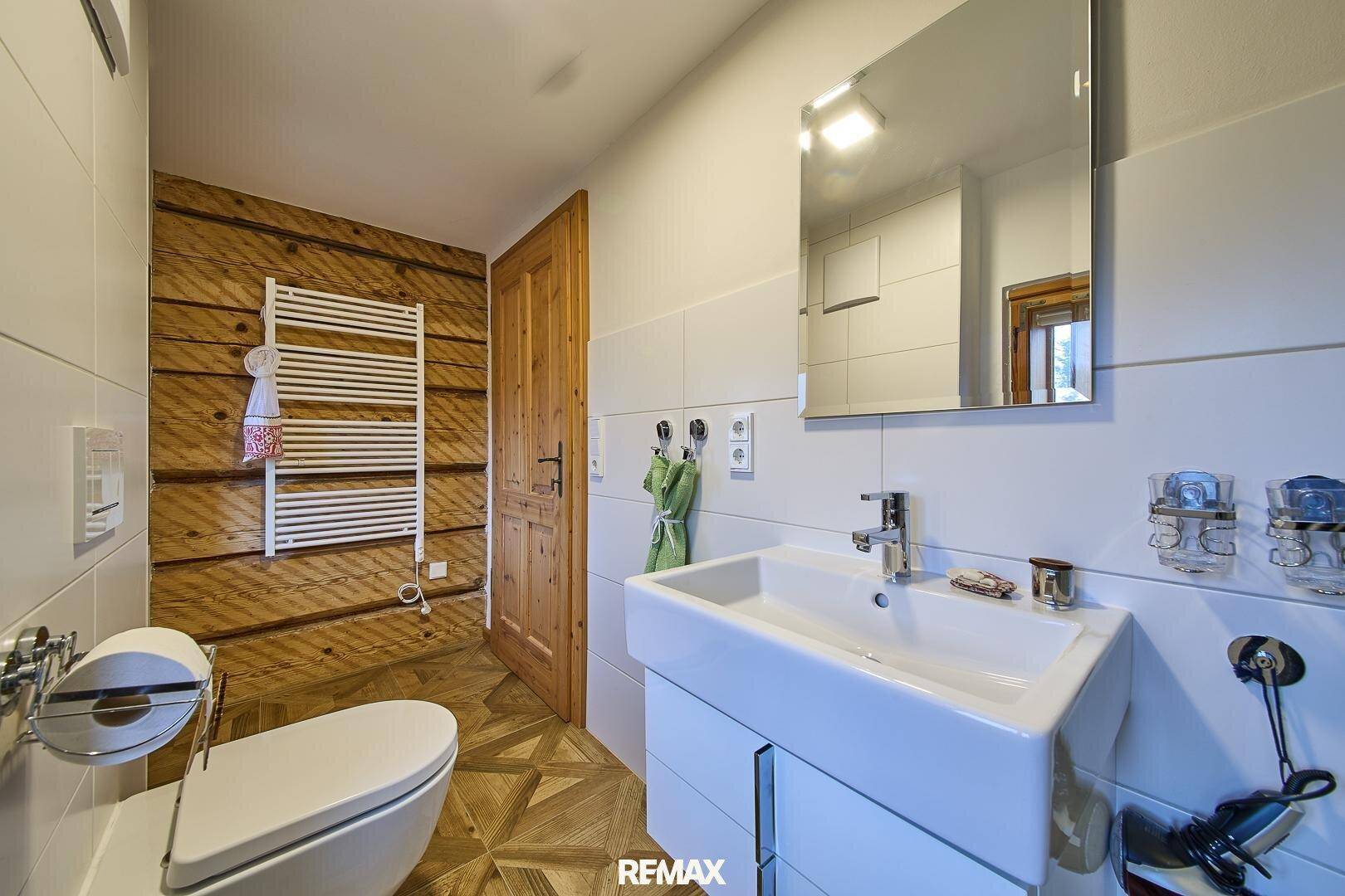 Helles Badezimmer mit WC, Waschbecken und beheiztem Handtuchhalter, kombiniert mit Holzelementen.