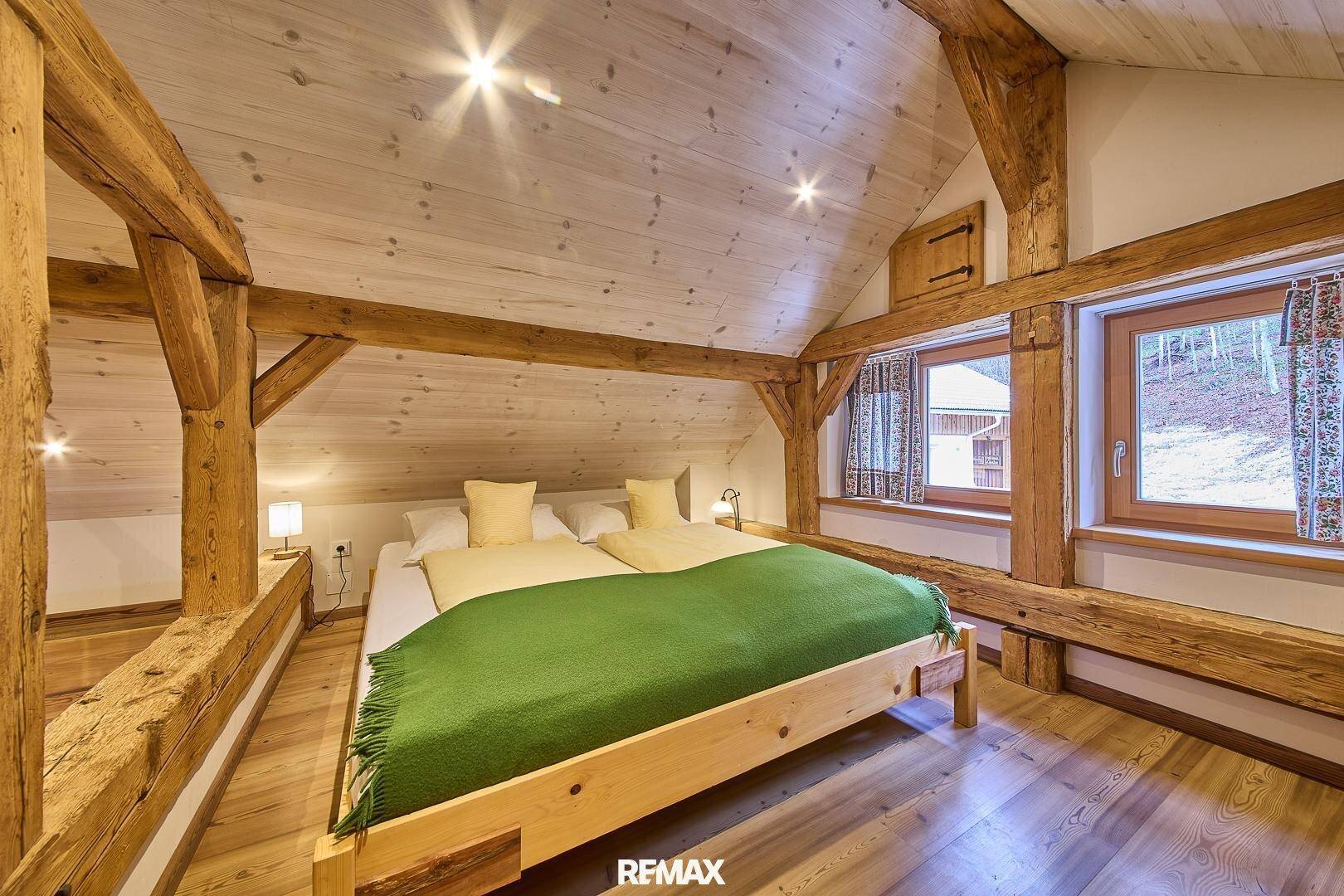 Helles Schlafzimmer im Dachgeschoss mit Holzbalken, Holzwänden und Blick ins Grüne.