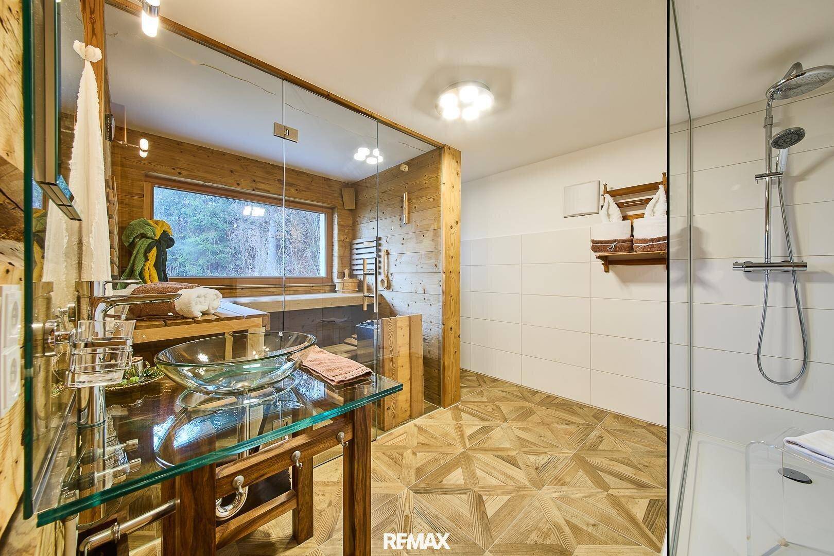 Modernes Badezimmer mit Sauna, Glaswaschbecken und begehbarer Dusche, umgeben von Holz.