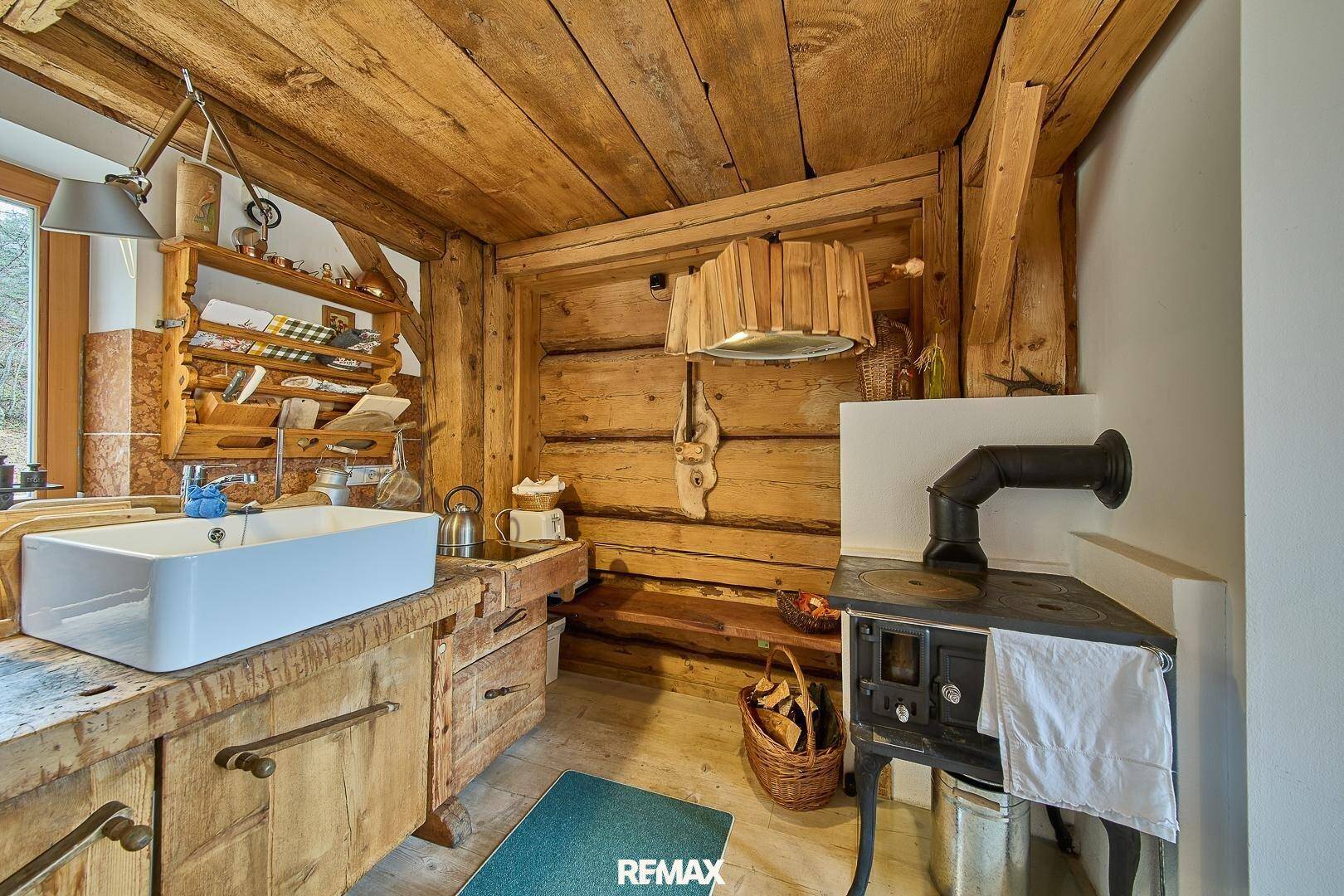 Rustikale Küche mit Holzarbeitsplatte, Spülbecken und traditionellem Holzofen, umgeben von Holzvertäfelung.
