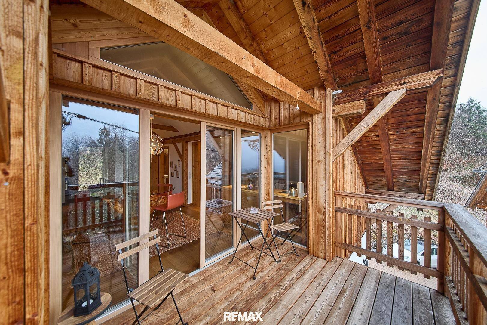 Rustikaler Holzbalkon mit Sitzgelegenheiten und Blick in den hellen Wohnbereich.
