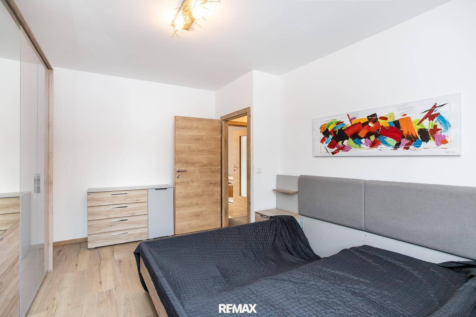Schlafzimmer mit Holzboden, modernem Bett und Kommode, bietet direkten Zugang zu weiteren Räumen.