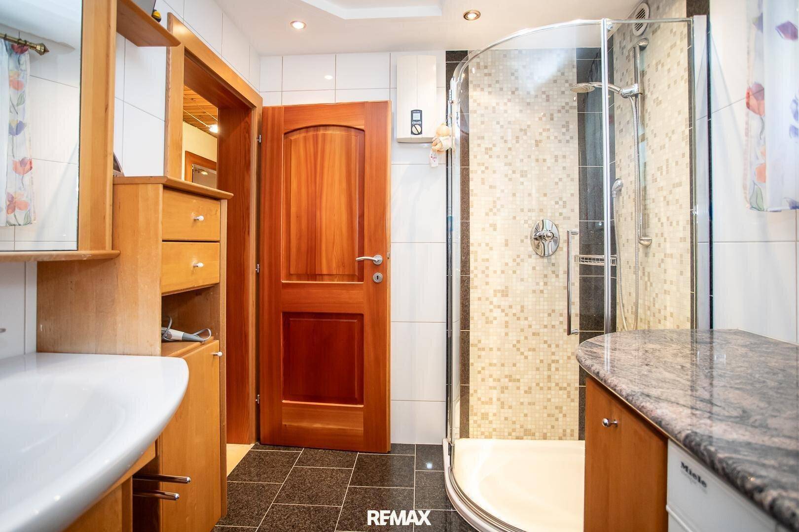 Badezimmer mit Duschkabine, Waschbecken und Holzelementen, gut beleuchtet.