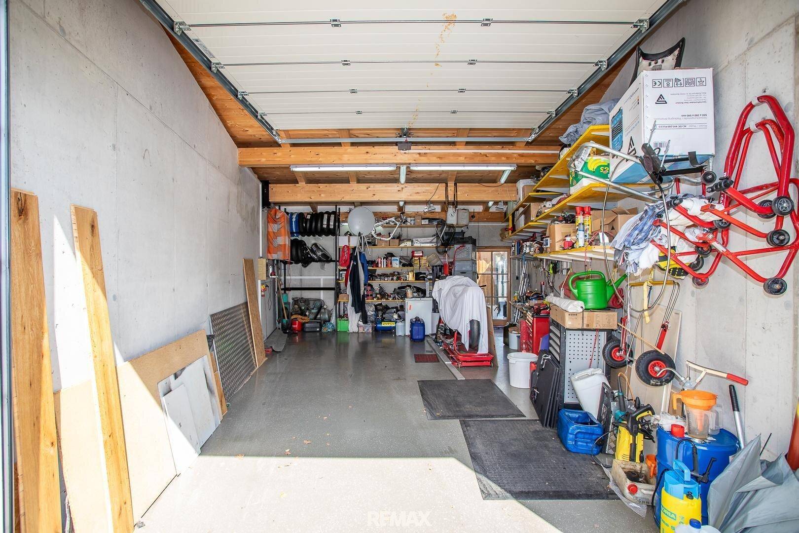 Geräumige Garage mit Betonboden, Lagerregalen und verschiedenen Werkzeugen und Geräten.