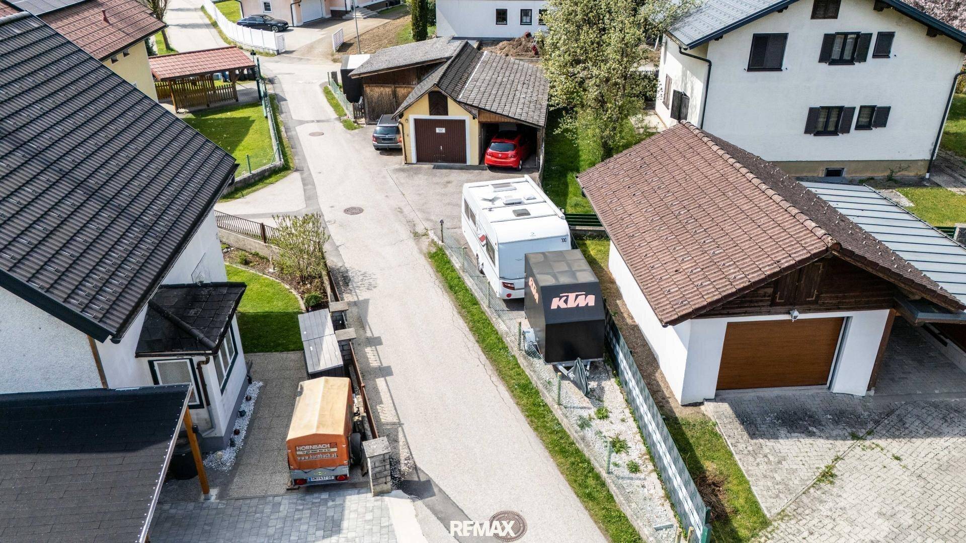 Luftaufnahme einer Wohnsiedlung mit Häusern, Garagen und einem Wohnwagen in ländlicher Umgebung.