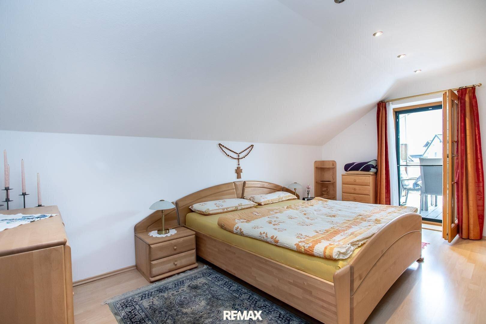Helles Schlafzimmer mit Holzbett, Parkettboden und direktem Zugang zum Balkon.