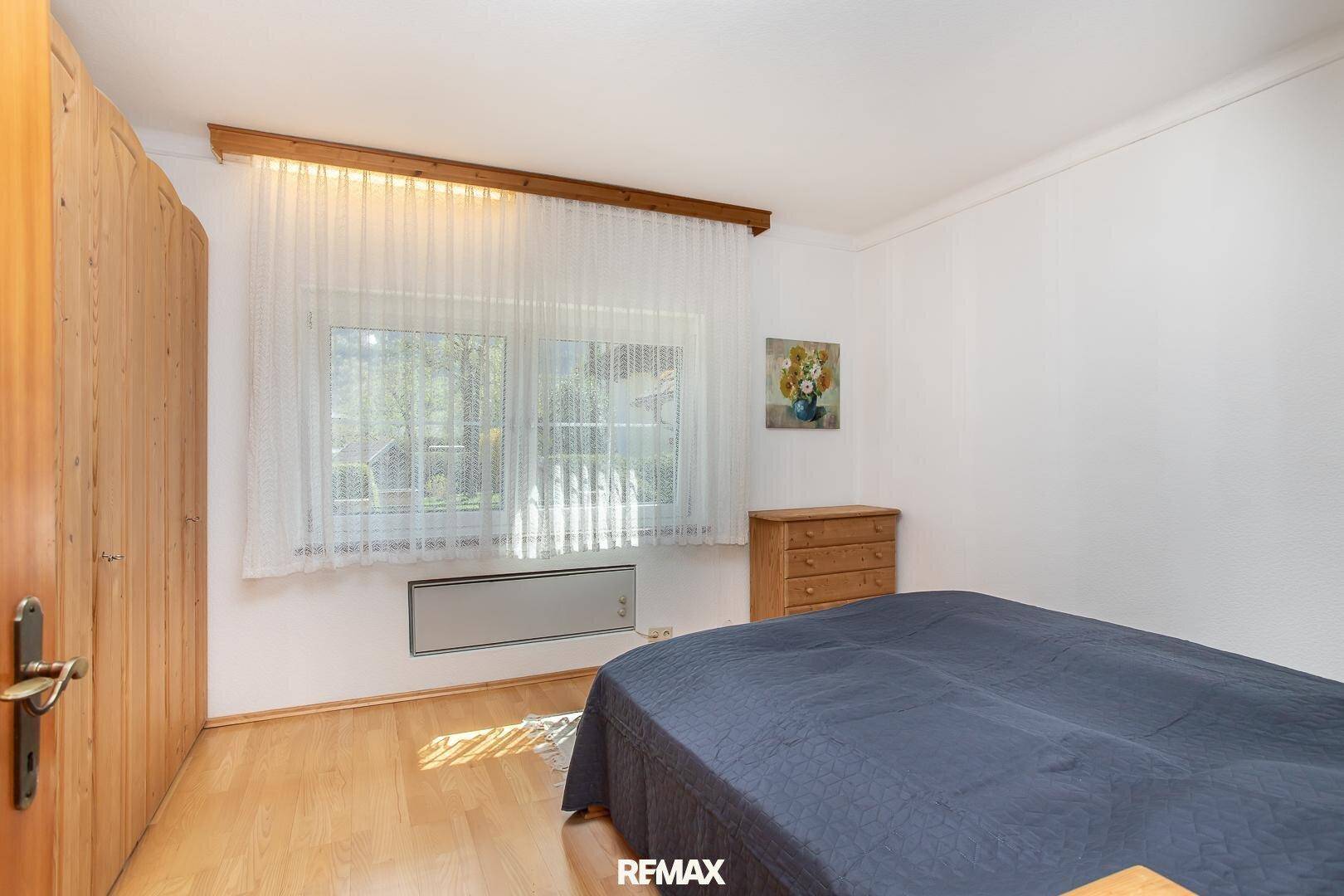 Helles Schlafzimmer mit Holzboden, großem Fenster und schlichten Möbeln.