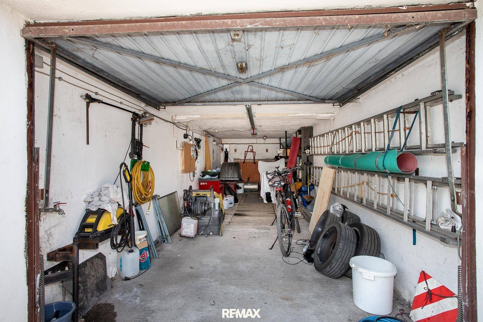 Einfache Garage mit Betonboden, Lagerregalen und verschiedenen Werkzeugen und Reifen.