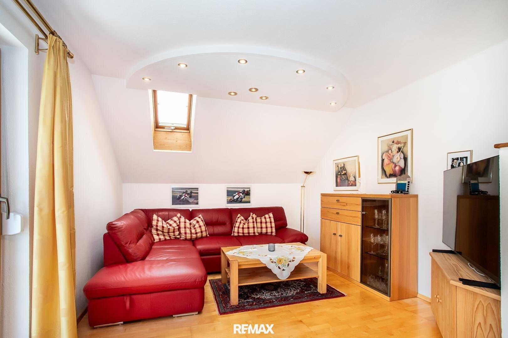 Heller Wohnbereich mit rotem Sofa, Dachfenster und Holzboden unter einer gewölbten Decke.
