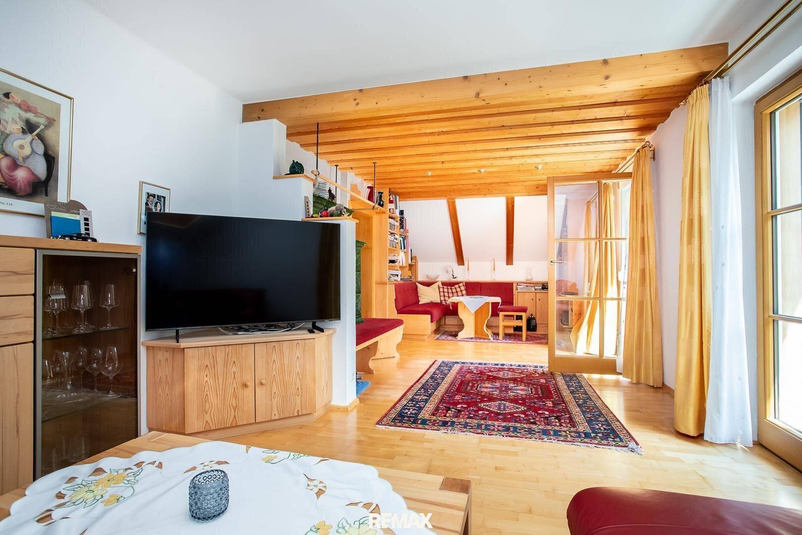 Geräumiges Wohnzimmer mit Holzbalkendecke, Parkettboden und Blick auf den Außenbereich.