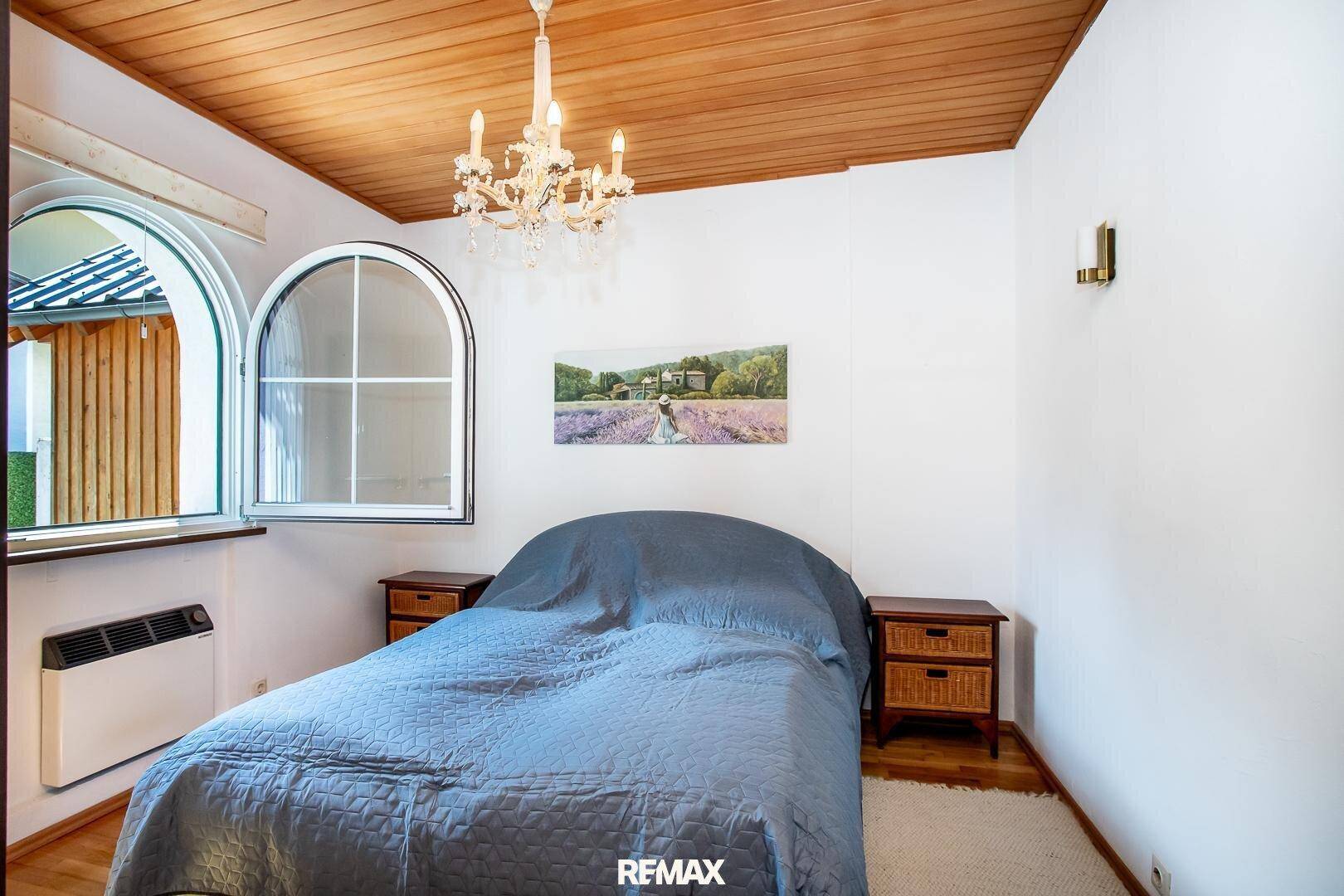 Schlafzimmer mit Holzbalkendecke, weiß gestrichenen Wänden und Bogenfenster.