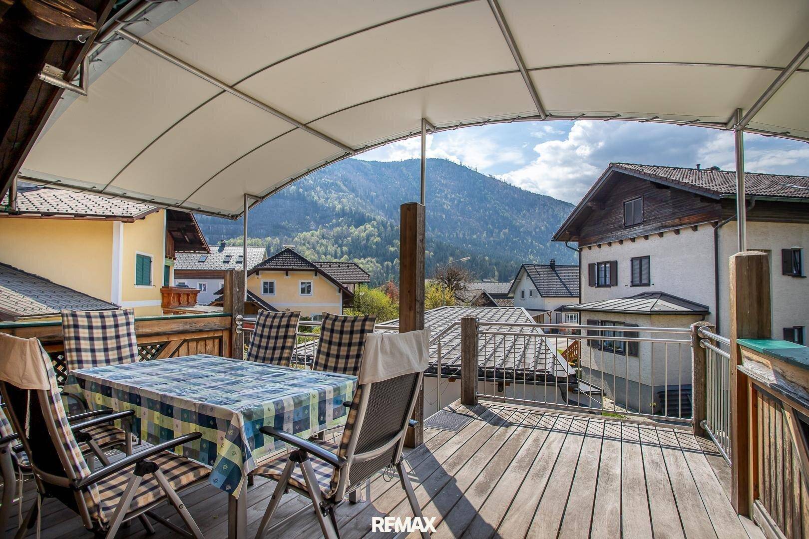 Geräumiger Balkon mit Holzboden, Esstisch und Stühlen, überdacht mit Bergblick.