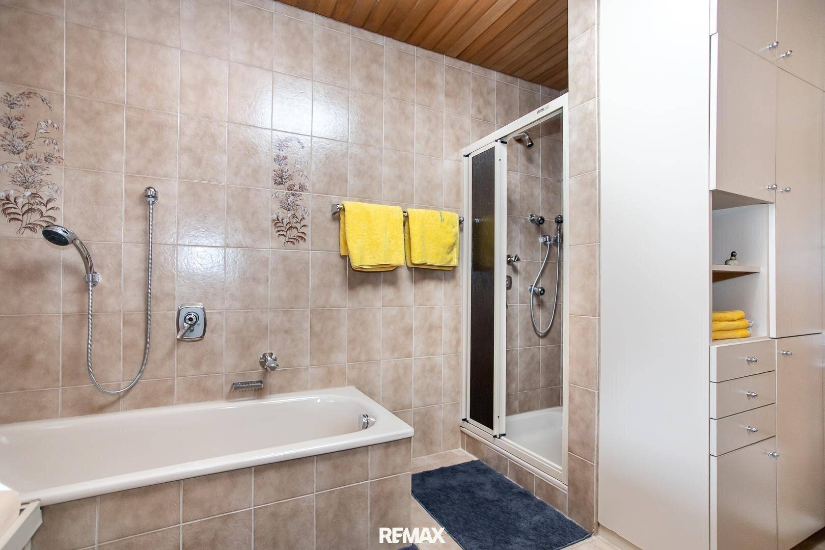 Gefliestes Badezimmer mit Badewanne, Duschkabine und integrierten Schränken.