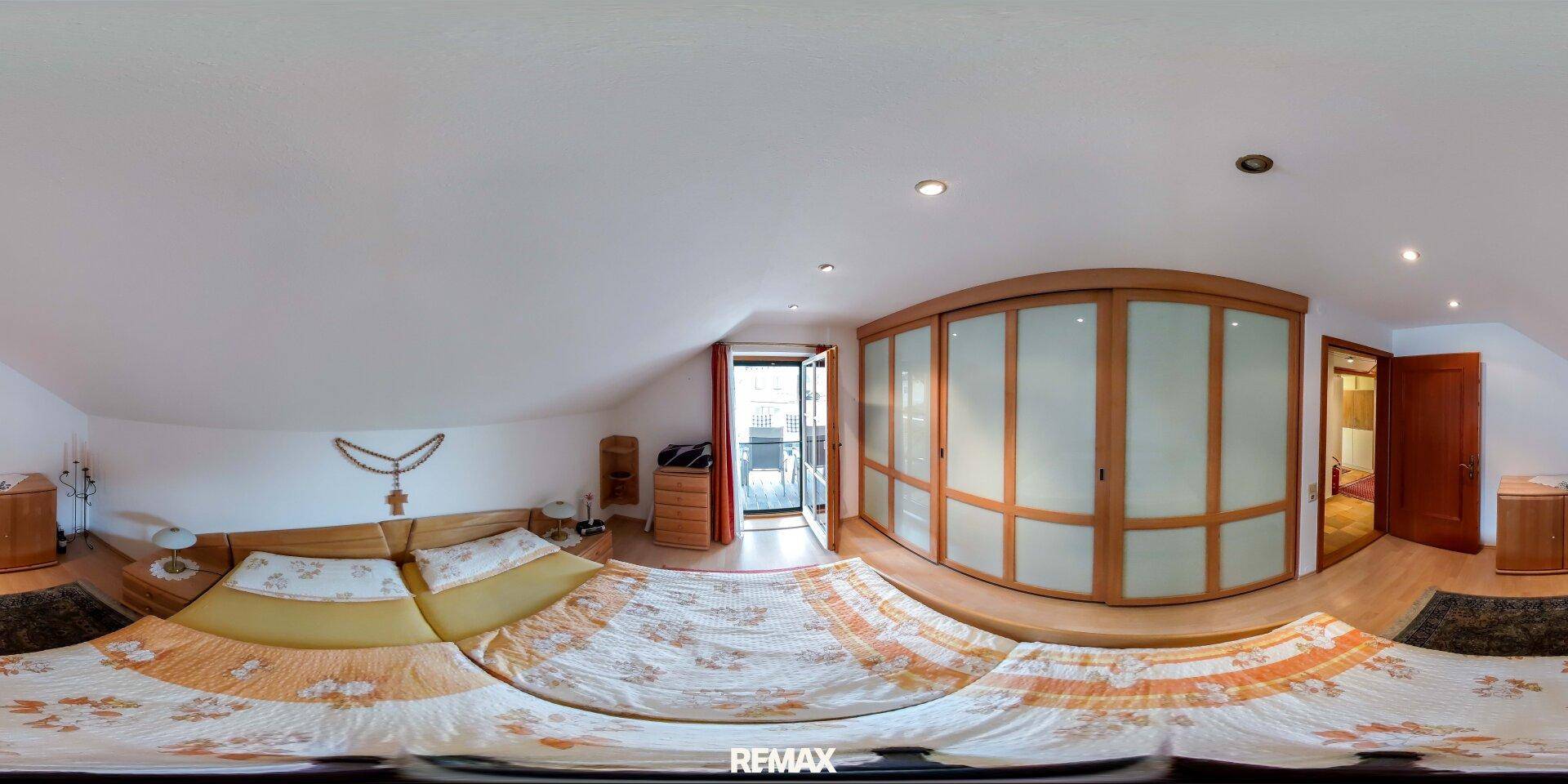 Schlafzimmer im Dachgeschoss mit schrägen Wänden, Holzboden und großem Kleiderschrank.