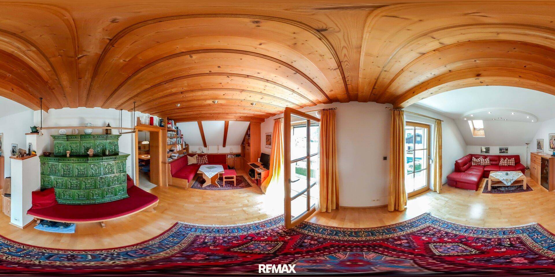 Gemütliches Wohnzimmer mit Holzbalkendecke, Kachelofen, Holzboden und Zugang zum Balkon.