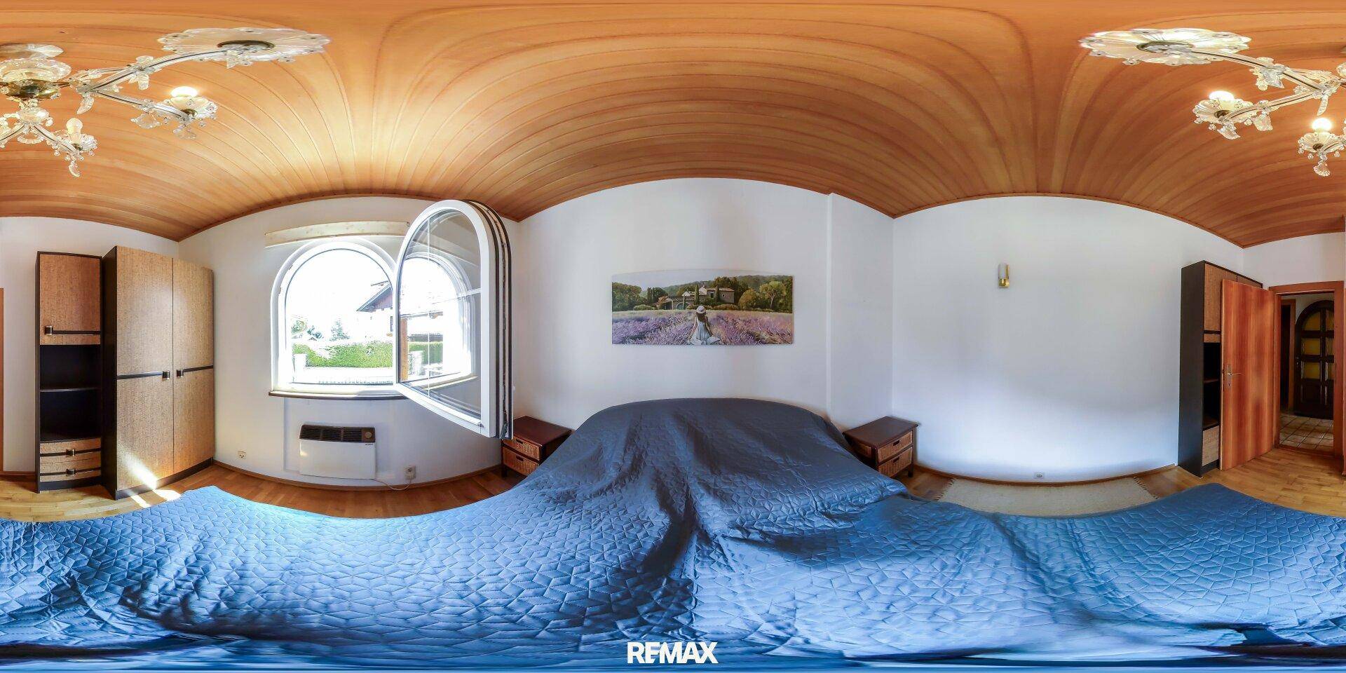 Helles Schlafzimmer mit Holzbalkendecke, Holzboden, großem Fenster und blauer Bettwäsche.