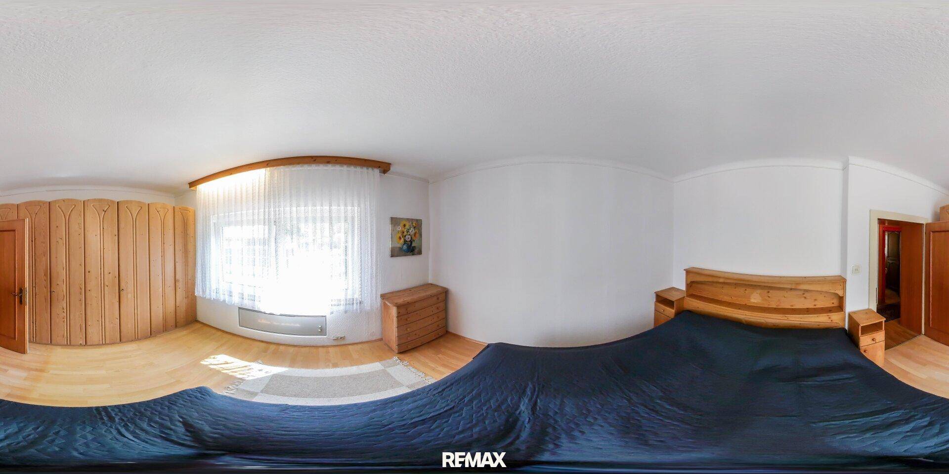 Schlafzimmer mit Holzboden, Einbauschränken und einem großen Fenster mit Vorhängen.