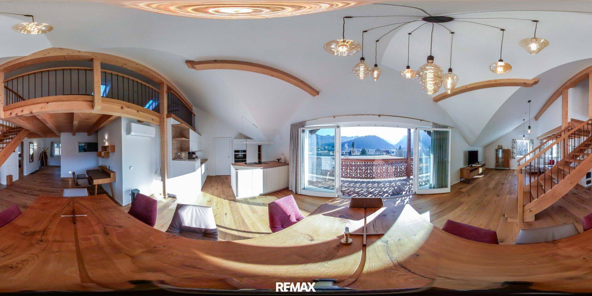 Panoramaaufnahme des offenen Wohn- und Essbereichs mit Küche, Holzbalken und Balkonzugang.