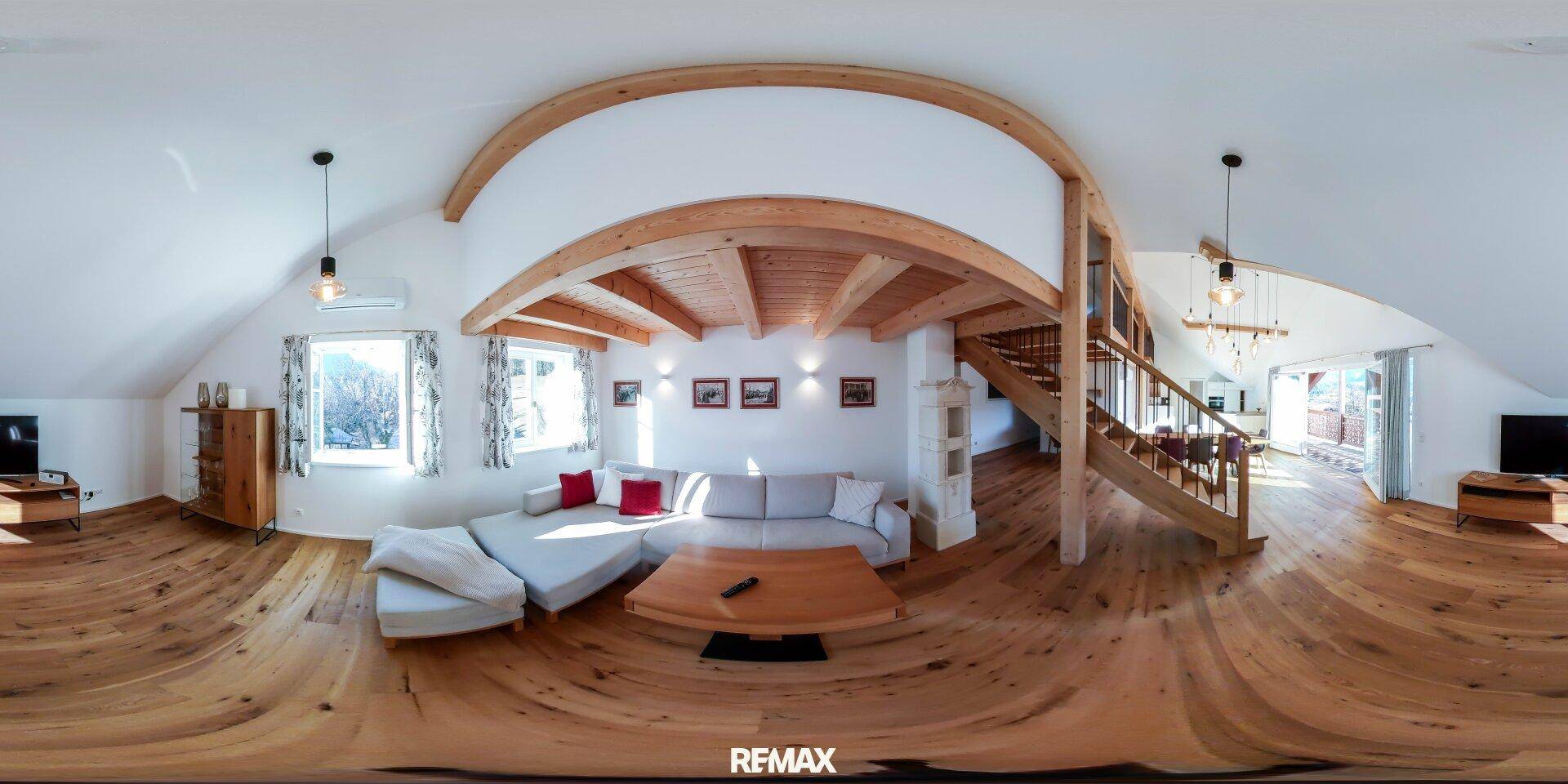Gemütliches Wohnzimmer mit Holzboden, sichtbaren Deckenbalken und einer bequemen Sitzecke unter dem Dach.