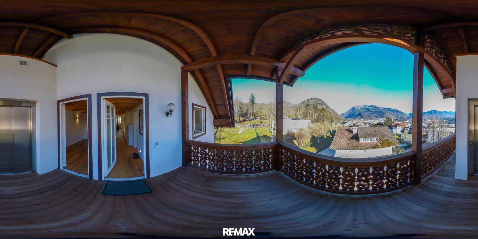 Großer Holzbalkon mit kunstvollem Geländer und Panoramablick auf die umliegende Berglandschaft.