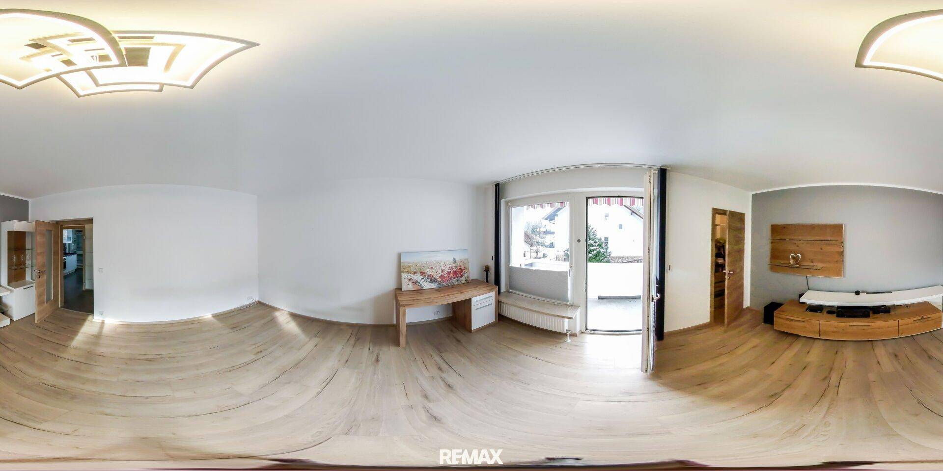 Panoramaansicht eines hellen Wohnzimmers mit Holzboden, moderner Einrichtung und Balkonzugang.