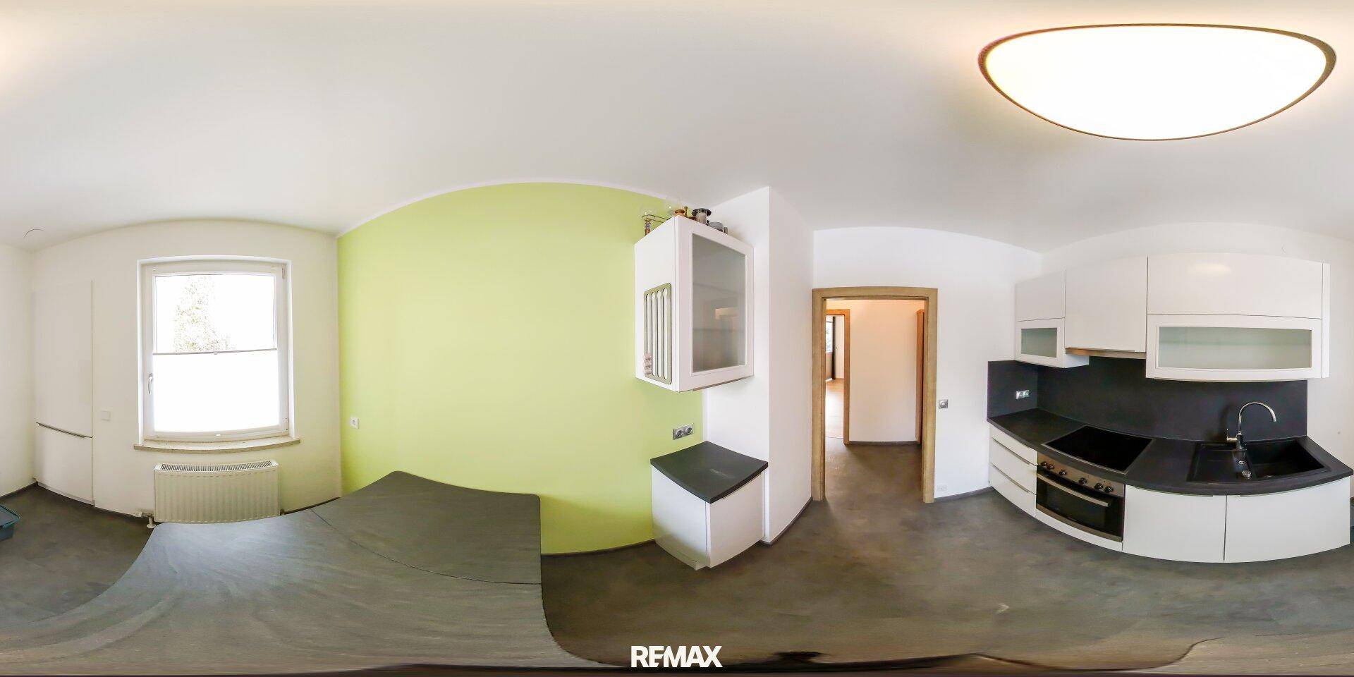 Panoramaansicht einer modernen Küche mit weißen Schränken, dunkler Arbeitsplatte und Essbereich.