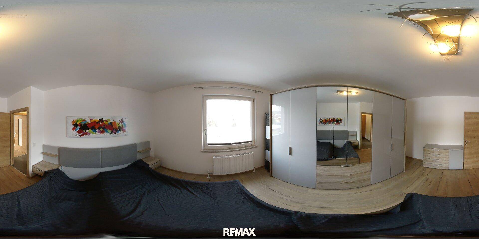 Panoramaansicht eines gemütlichen Schlafzimmers mit Holzboden, großem Bett und Spiegelschrank.