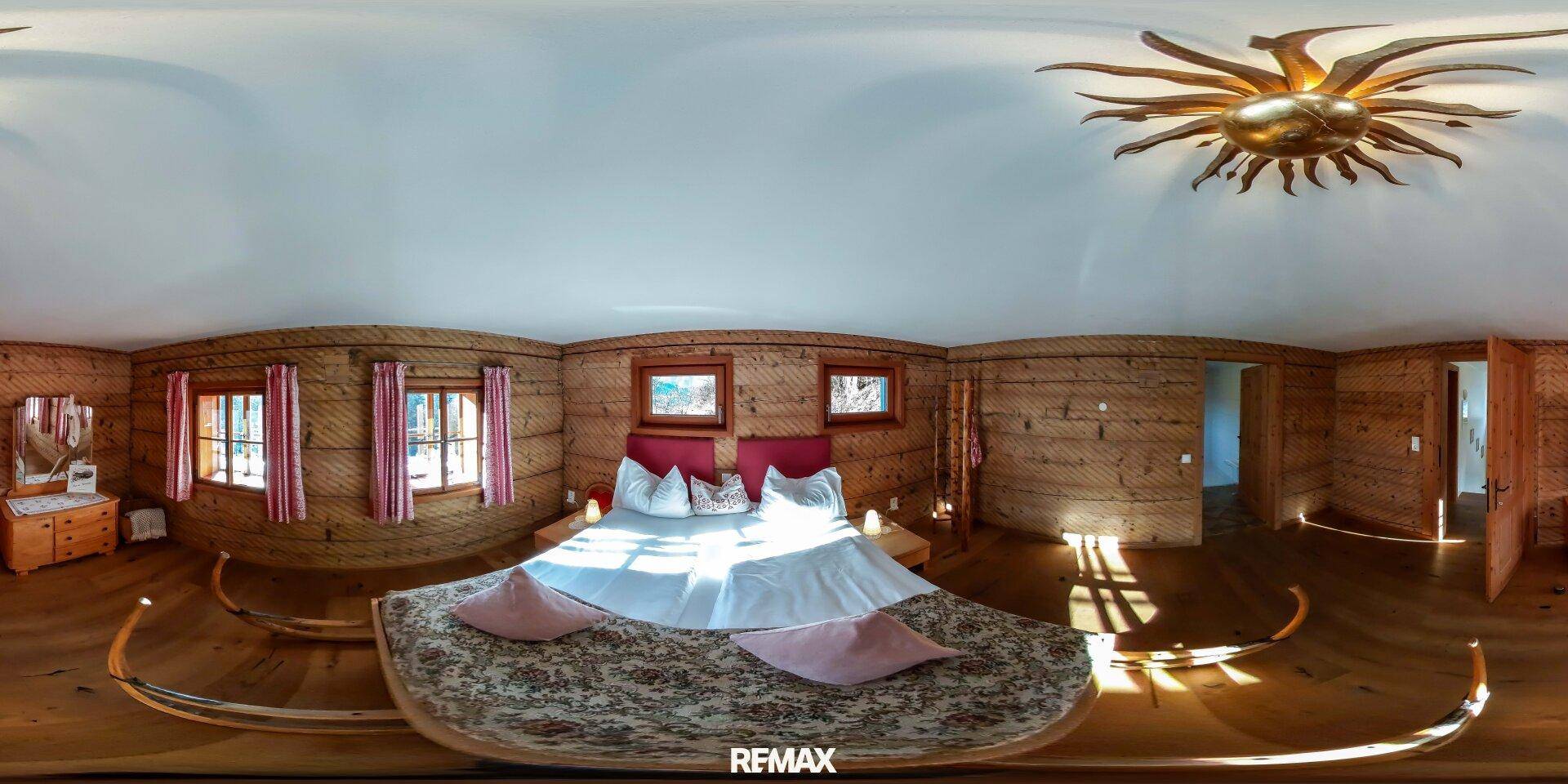 Rustikales Schlafzimmer mit Holzwänden, Doppelbett und dekorativer Deckenleuchte.