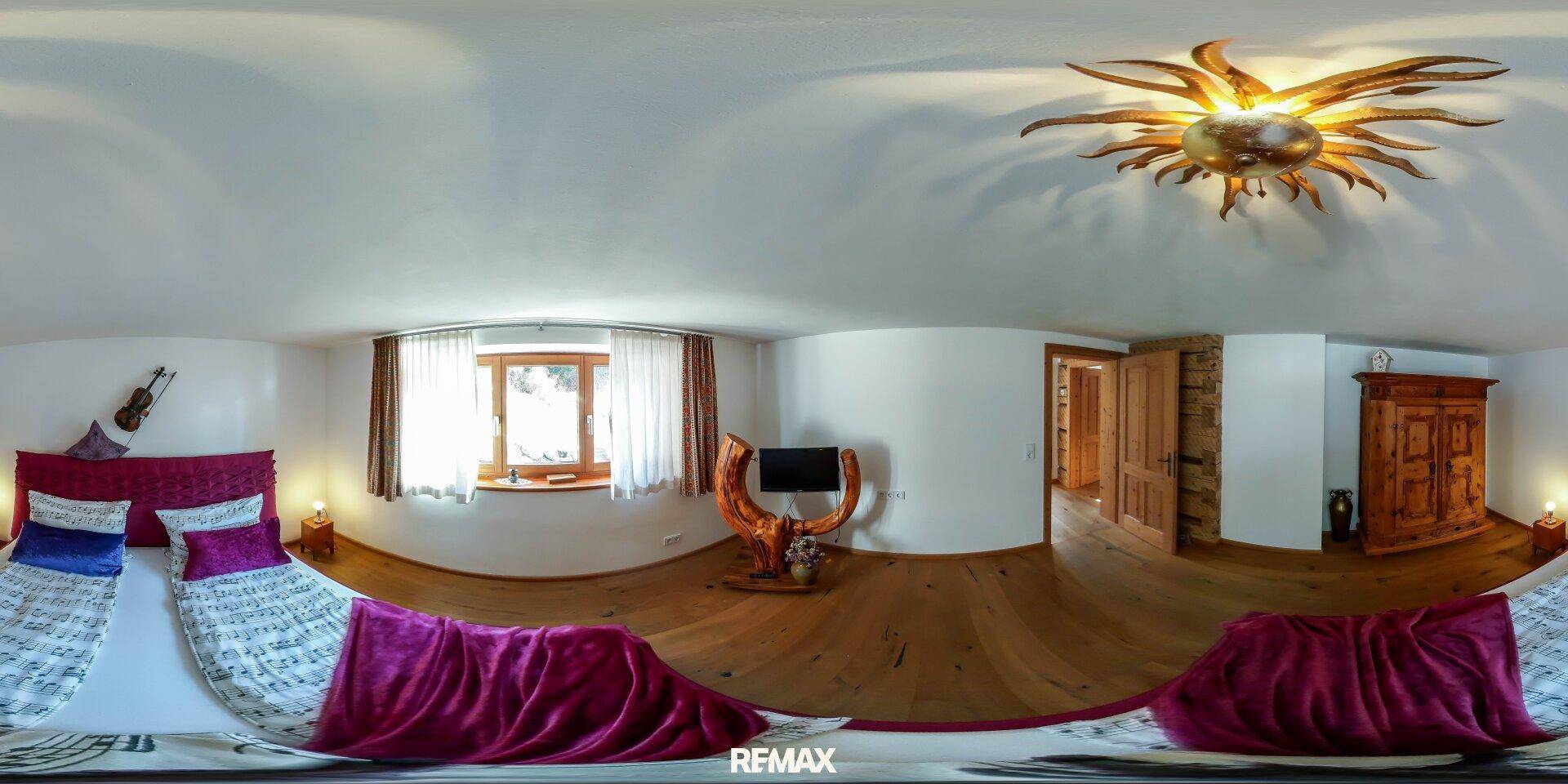 Gemütliches Schlafzimmer mit Holzboden, einem großen Bett und dekorativer Deckenleuchte.