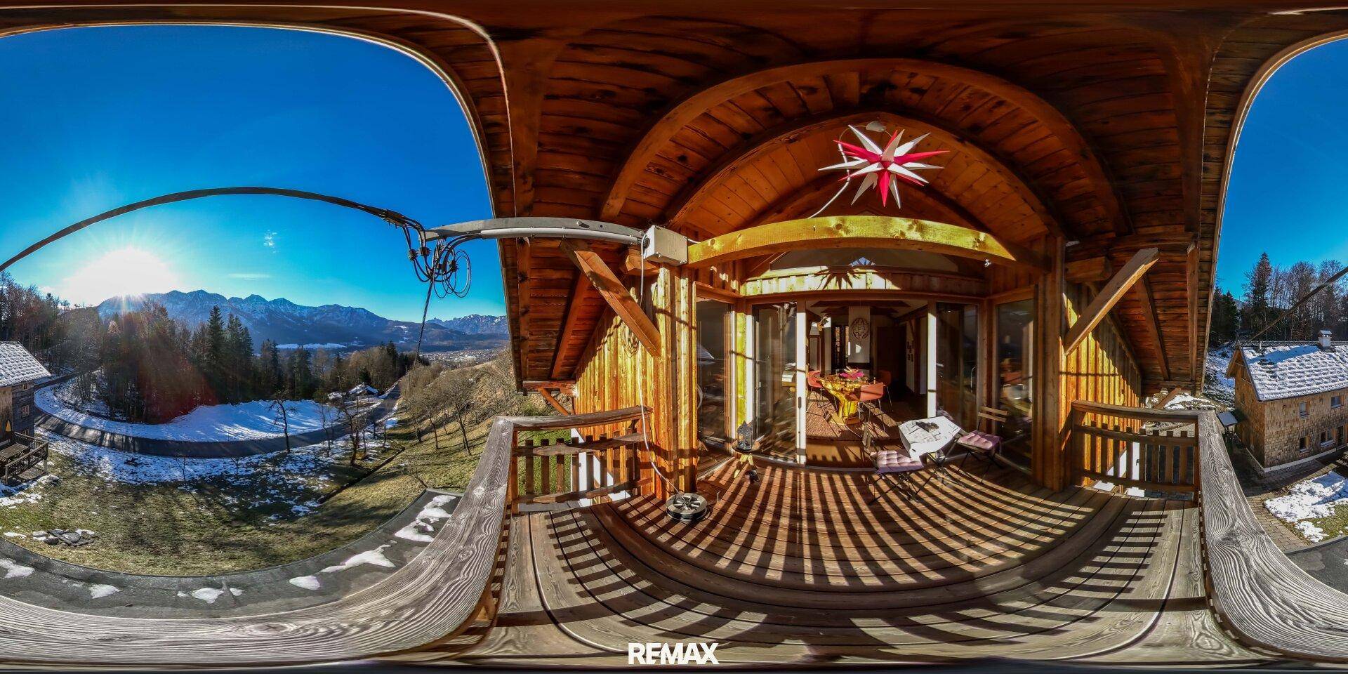 Großer Holzbalkon mit weitem Blick auf die Berge und die verschneite Landschaft an einem sonnigen Tag.