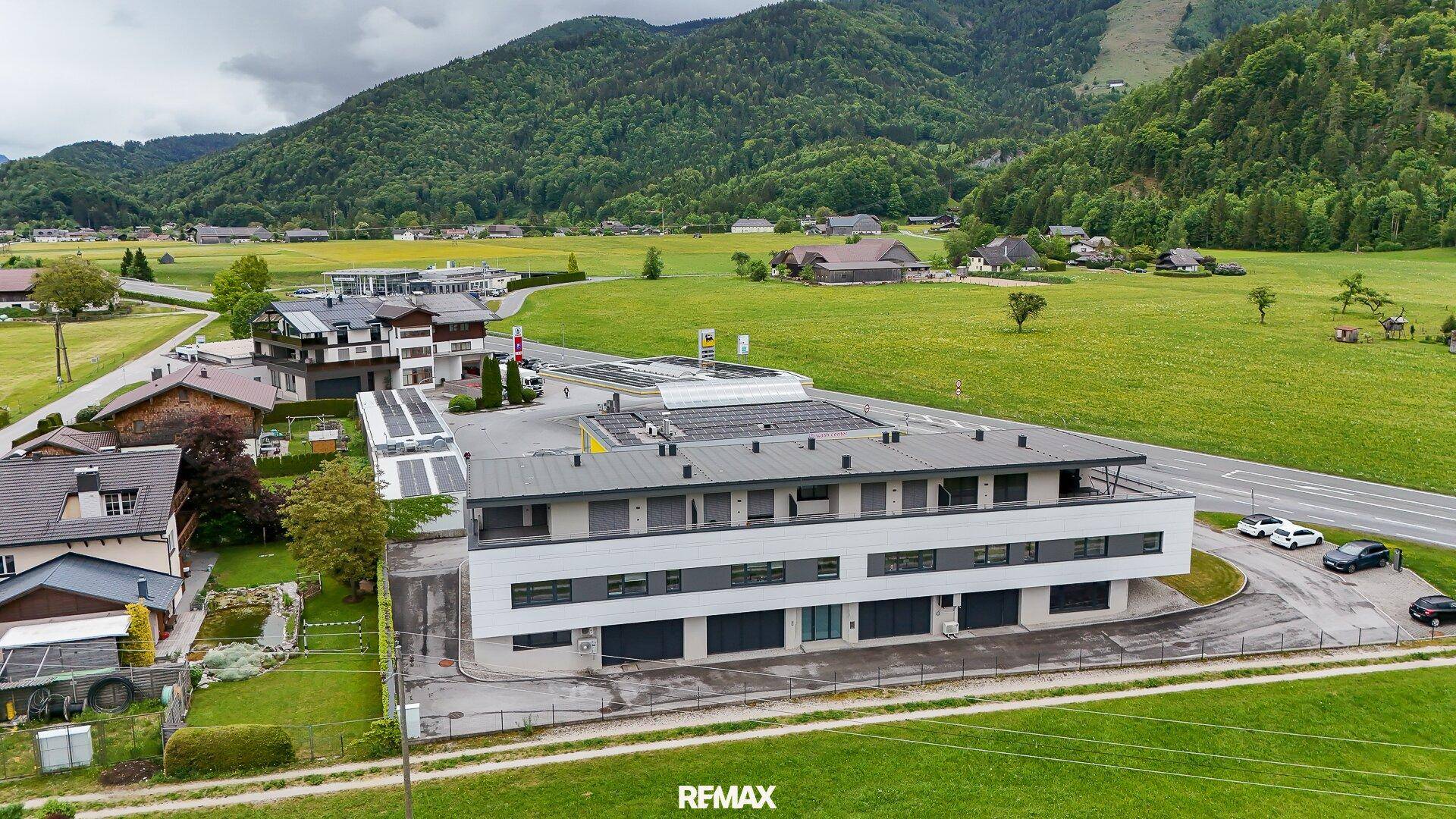 Weitläufige Luftaufnahme des Geschäftsgebäudes, eingebettet in grüne Felder mit Bergblick und einer Straße.