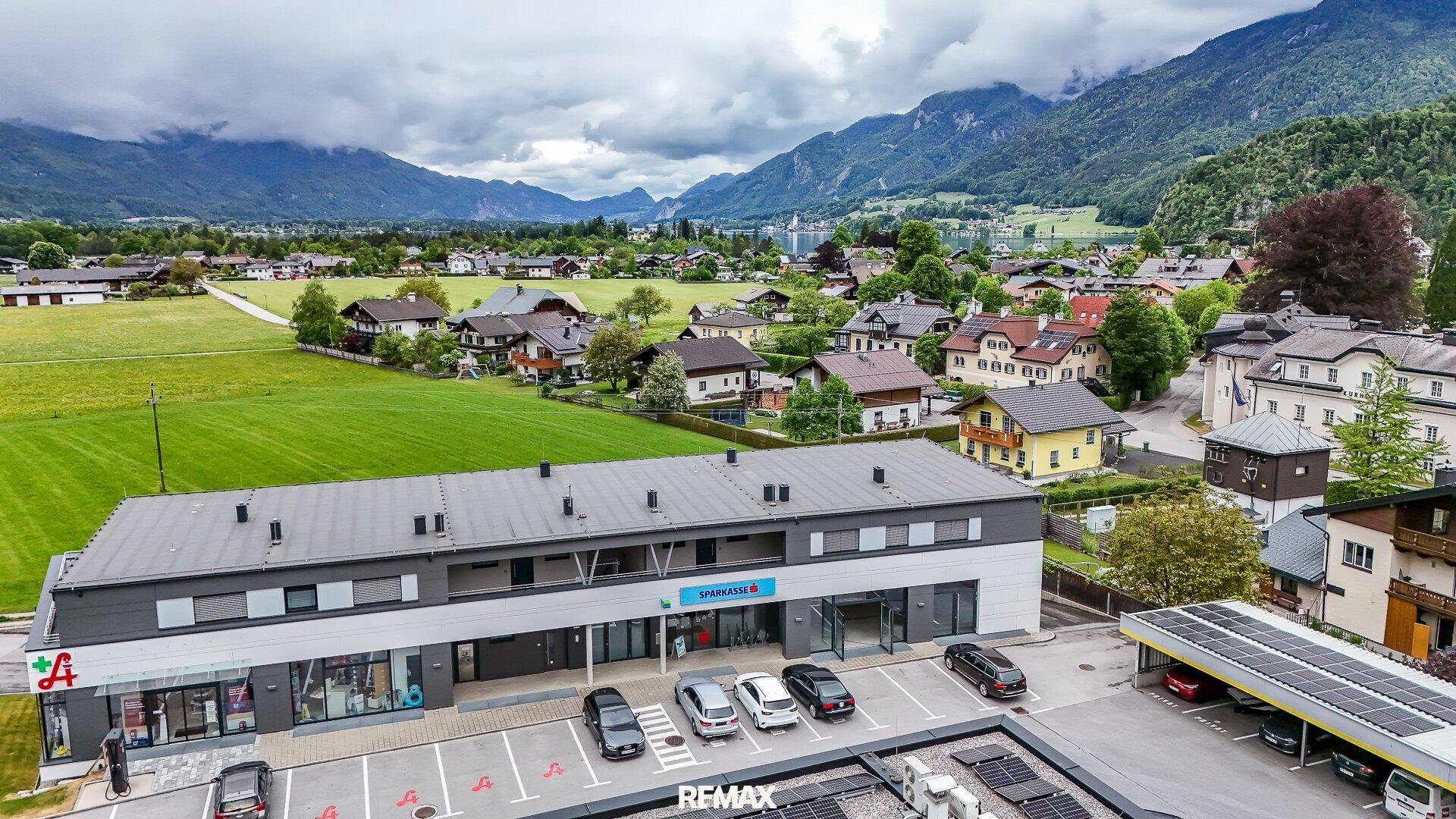 Luftaufnahme eines modernen Geschäftsgebäudes mit Parkplätzen, umgeben von grüner Landschaft und Bergen.