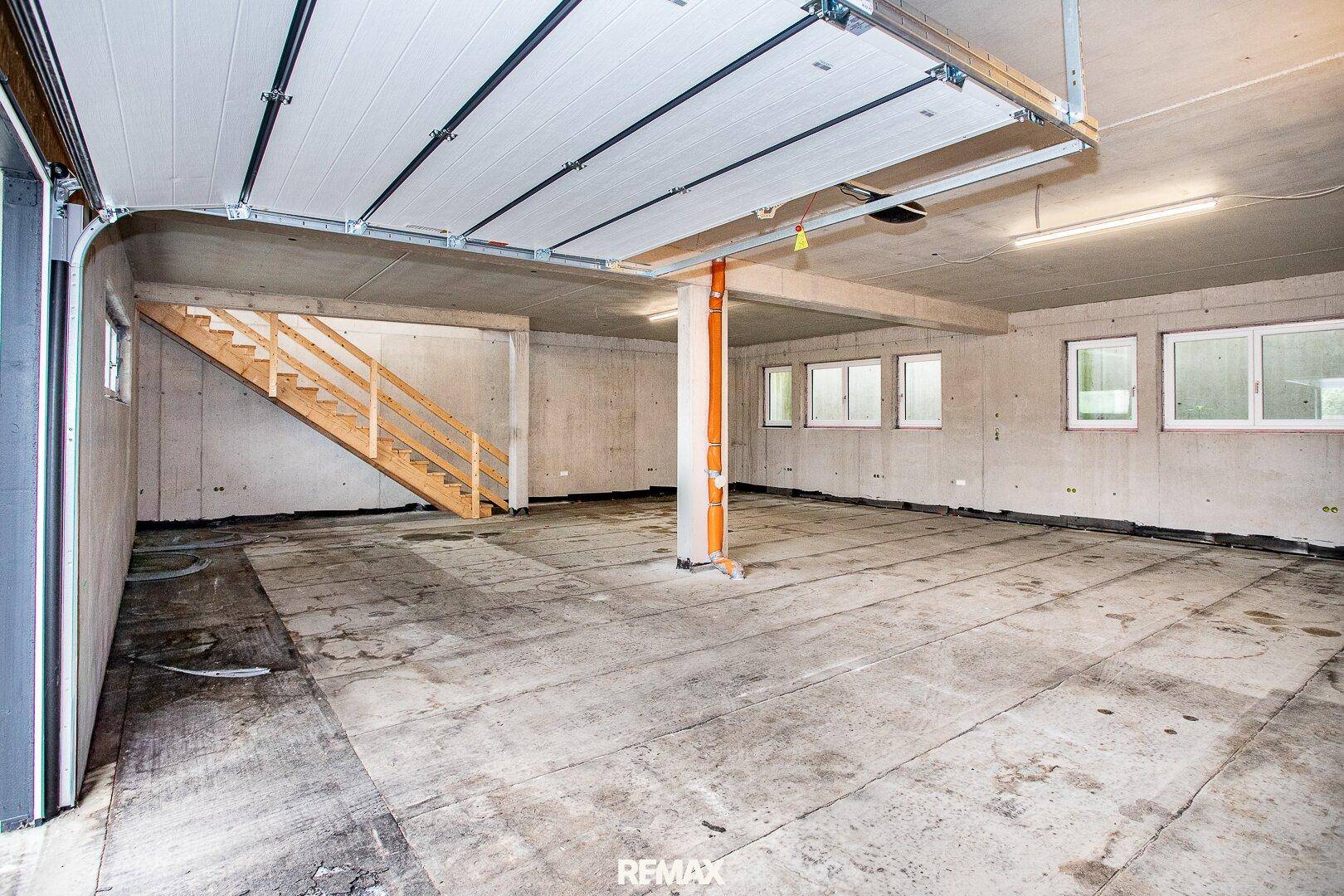 Großer Kellerraum oder Tiefgarage im Rohbau mit Betonboden, Treppe und Fenstern, bereit für den Ausbau.