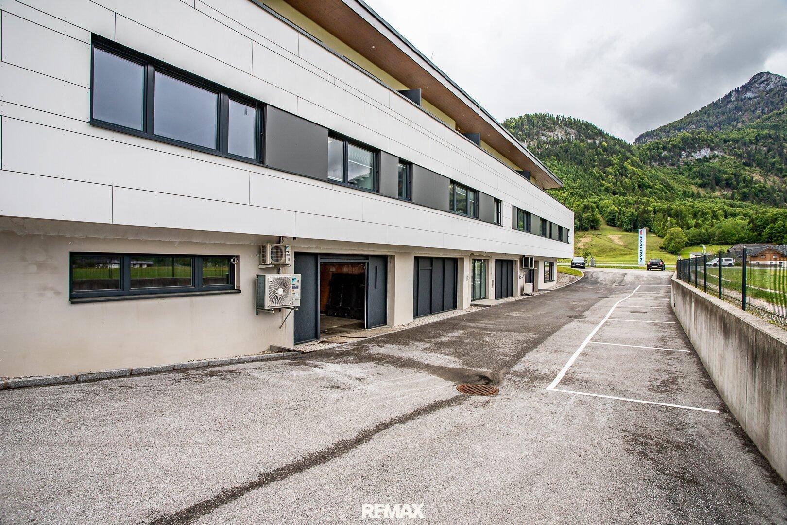 Seitenansicht des modernen Geschäftsgebäudes mit Parkplätzen, umgeben von grünen Hügeln und Bergen.