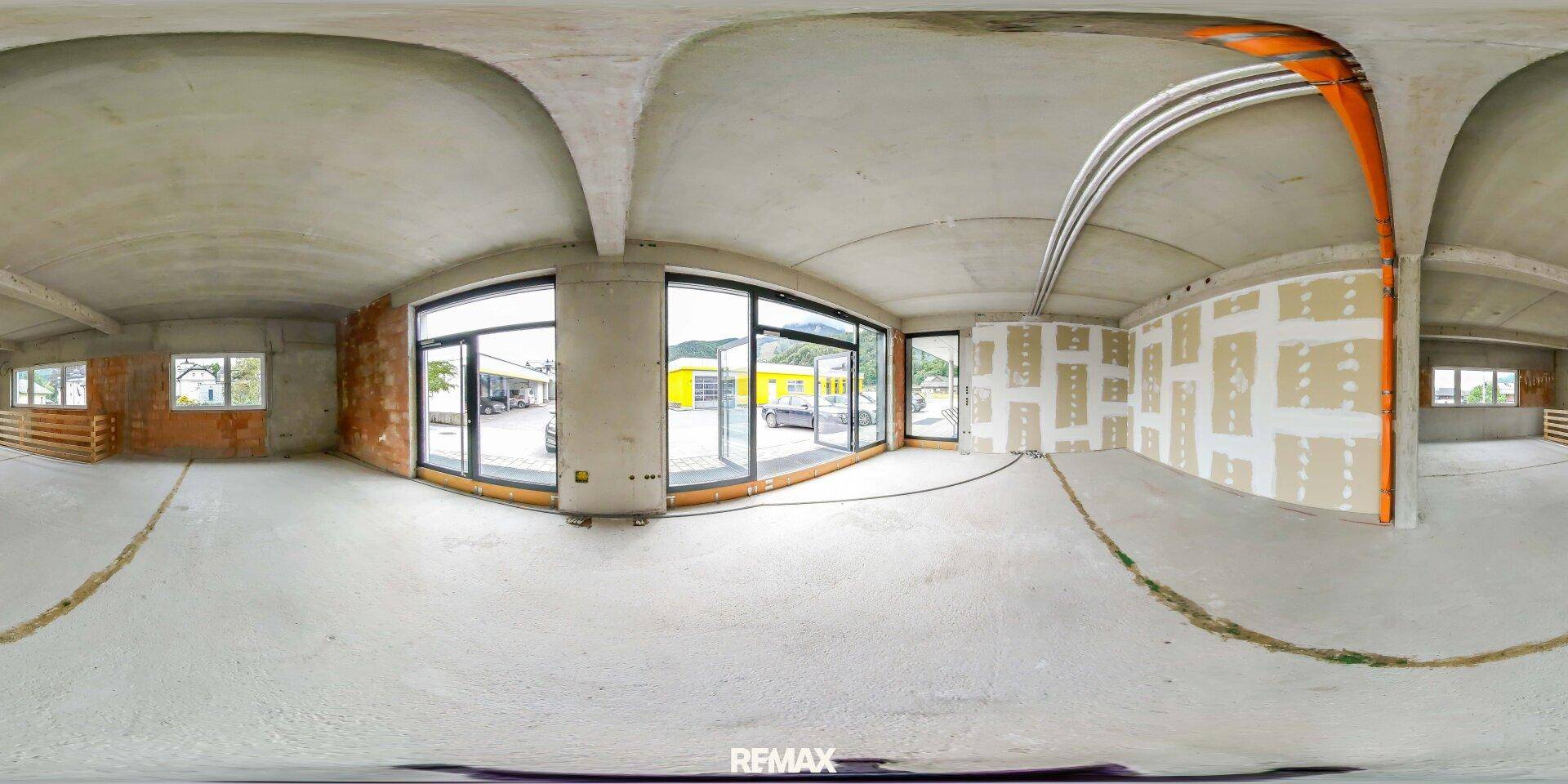 Panoramaansicht eines großen Gewerberaums im Rohbau mit Betonwänden, großen Fenstern und sichtbaren Installationen.