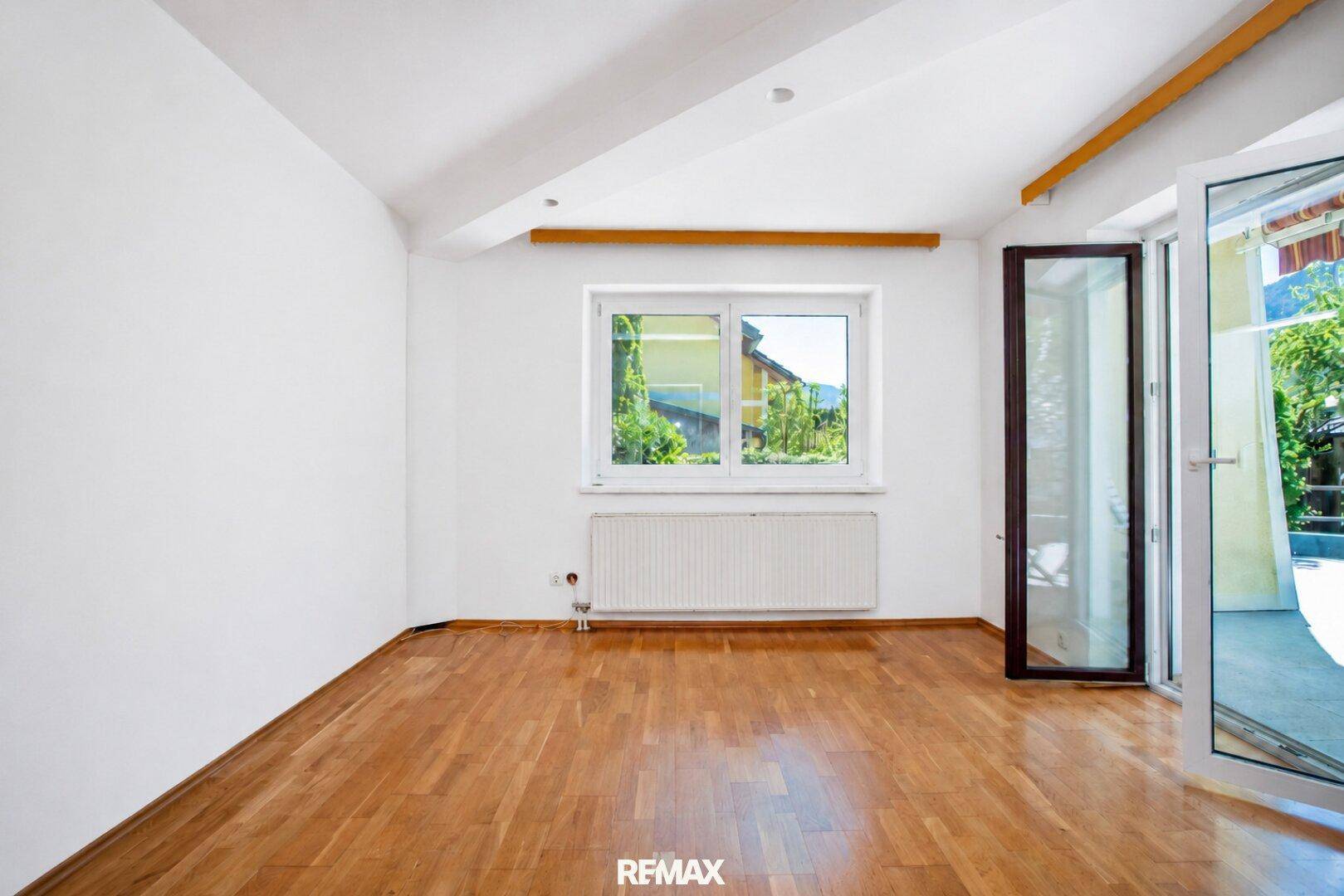 Helles Zimmer mit Holzboden, großem Fenster und Zugang zu einem Außenbereich.