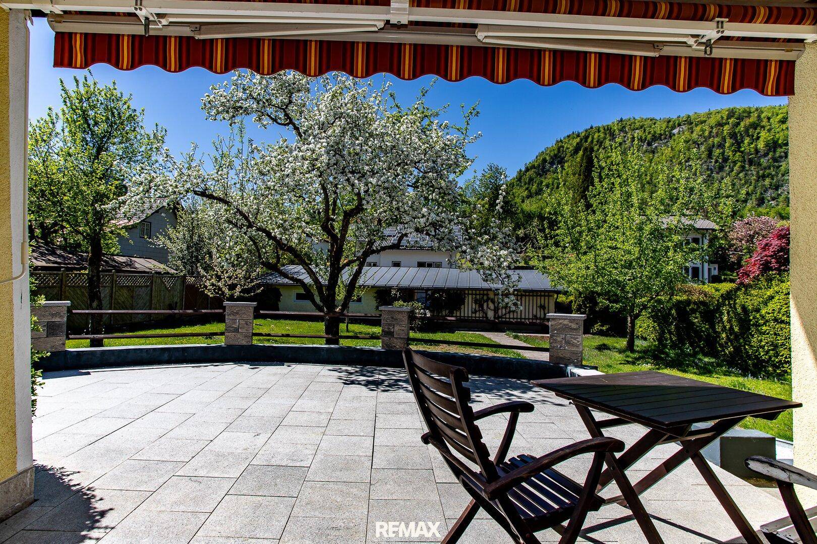 Sonniger Terrassenbereich mit Gartenmöbeln, Markise und Blick ins Grüne.