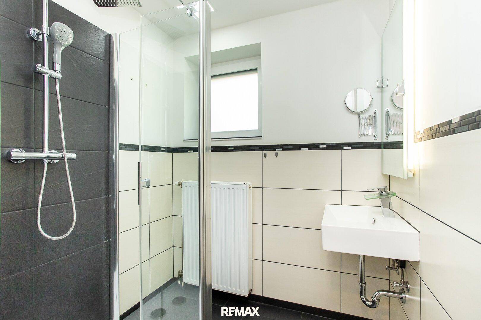 Modernes Badezimmer mit Duschkabine, Waschbecken und Fliesen in Schwarz-Weiß.