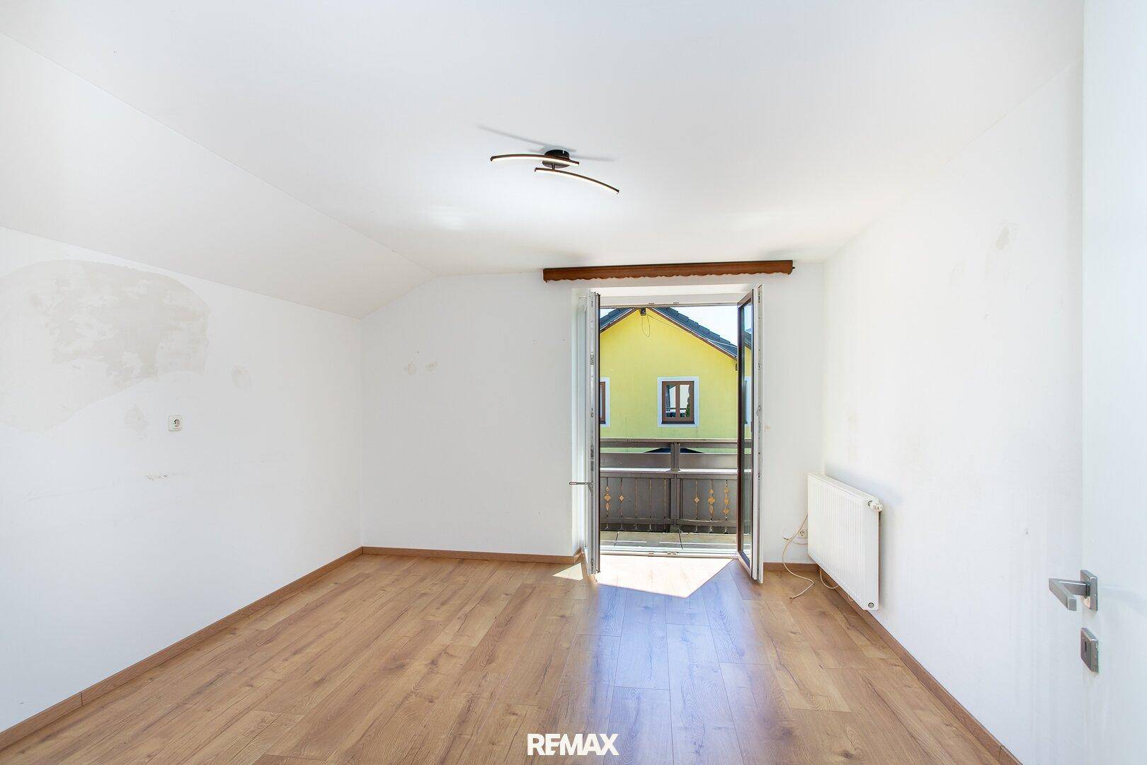 Helles Schlafzimmer mit Laminatboden und direktem Zugang zu einem Balkon.
