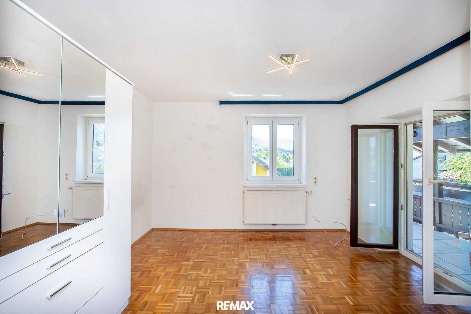 Geräumiges Schlafzimmer mit Parkettboden, Spiegelschrank und Balkonzugang.