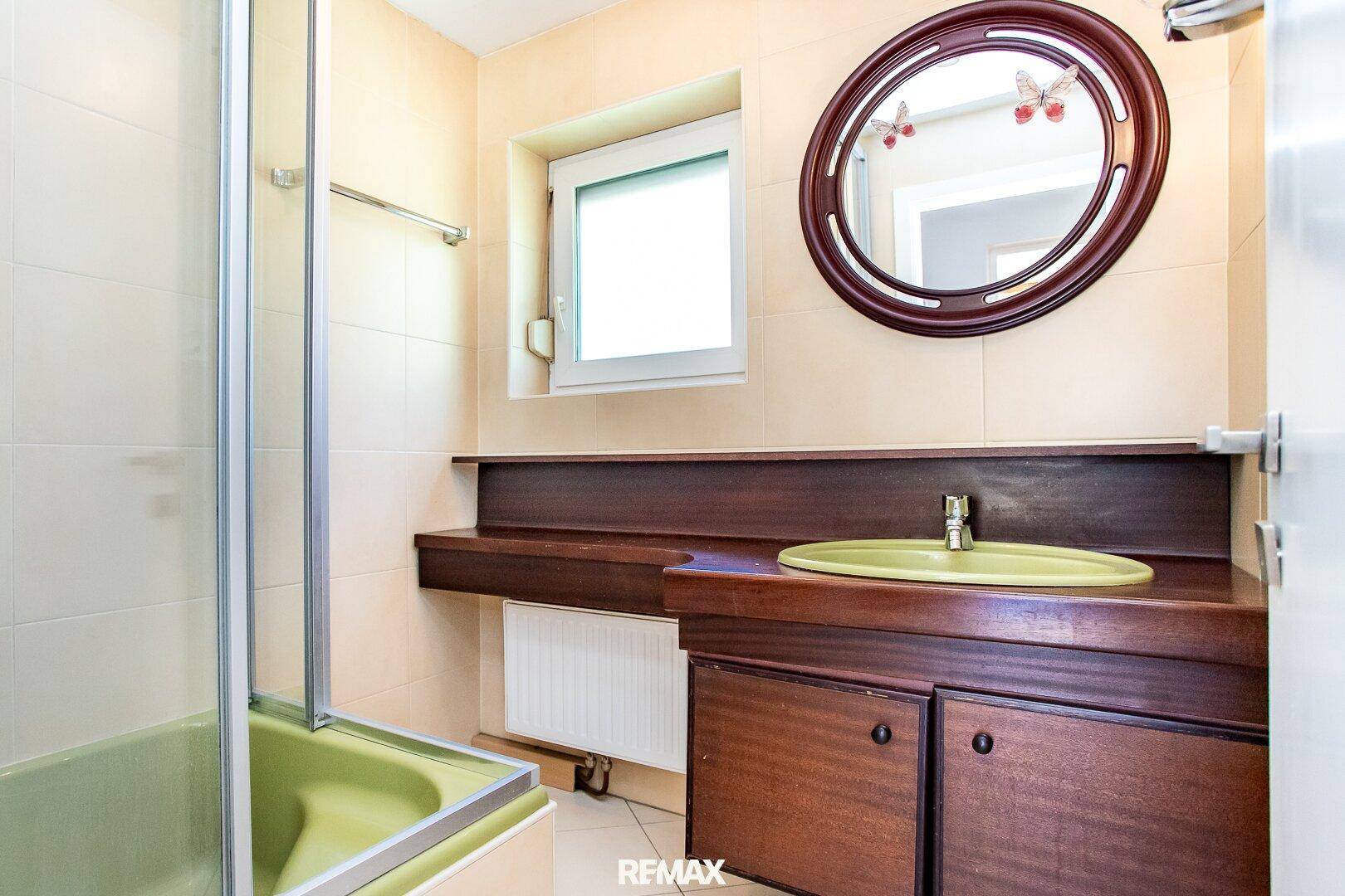 Badezimmer im älteren Stil mit grüner Badewanne, Waschbecken und Holzwaschtisch.