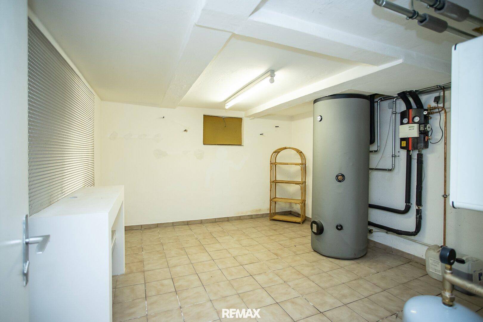 Technikraum im Keller mit Warmwasserspeicher, Heizungsanlage und Fliesenboden.