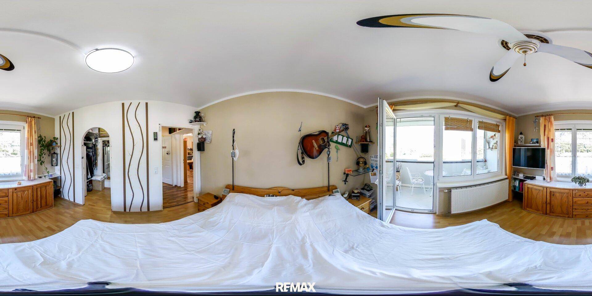 Panoramaansicht des hellen Schlafzimmers mit Holzbett, Deckenventilator und Balkonzugang.