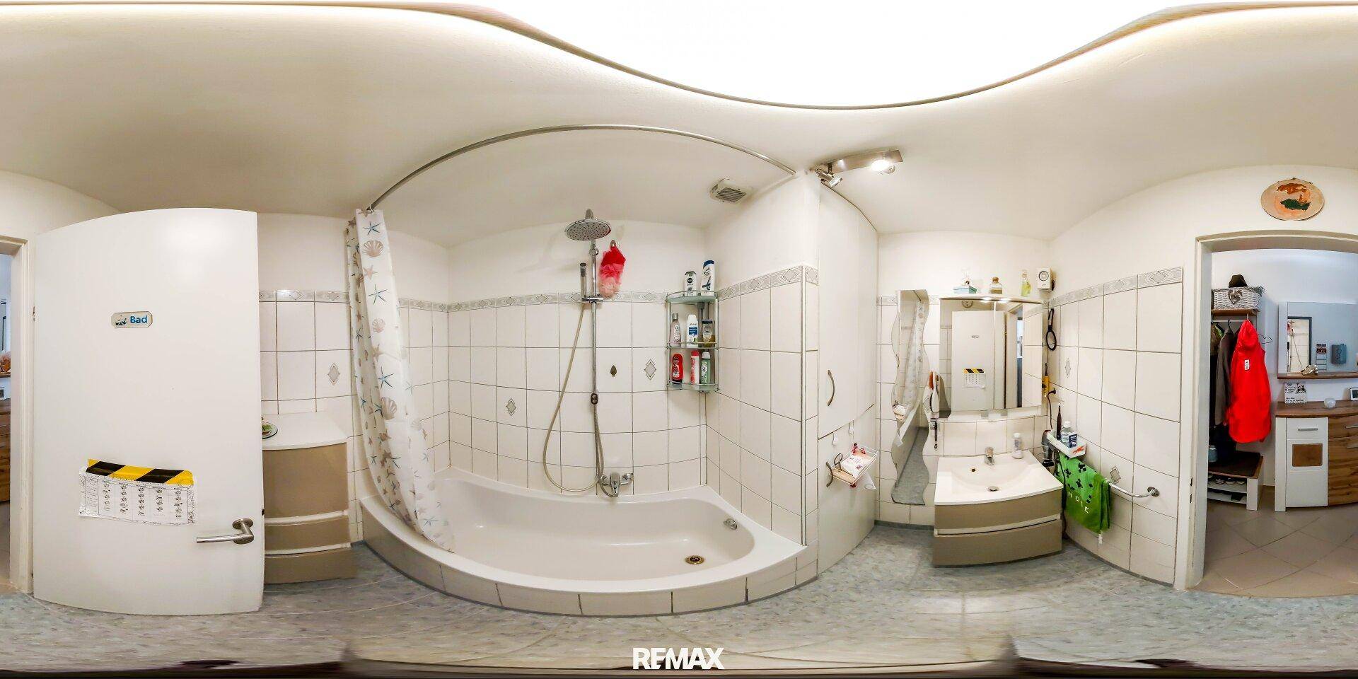 Panoramaansicht des Badezimmers mit Badewanne, Duschfunktion, Waschbecken und weißen Fliesen.