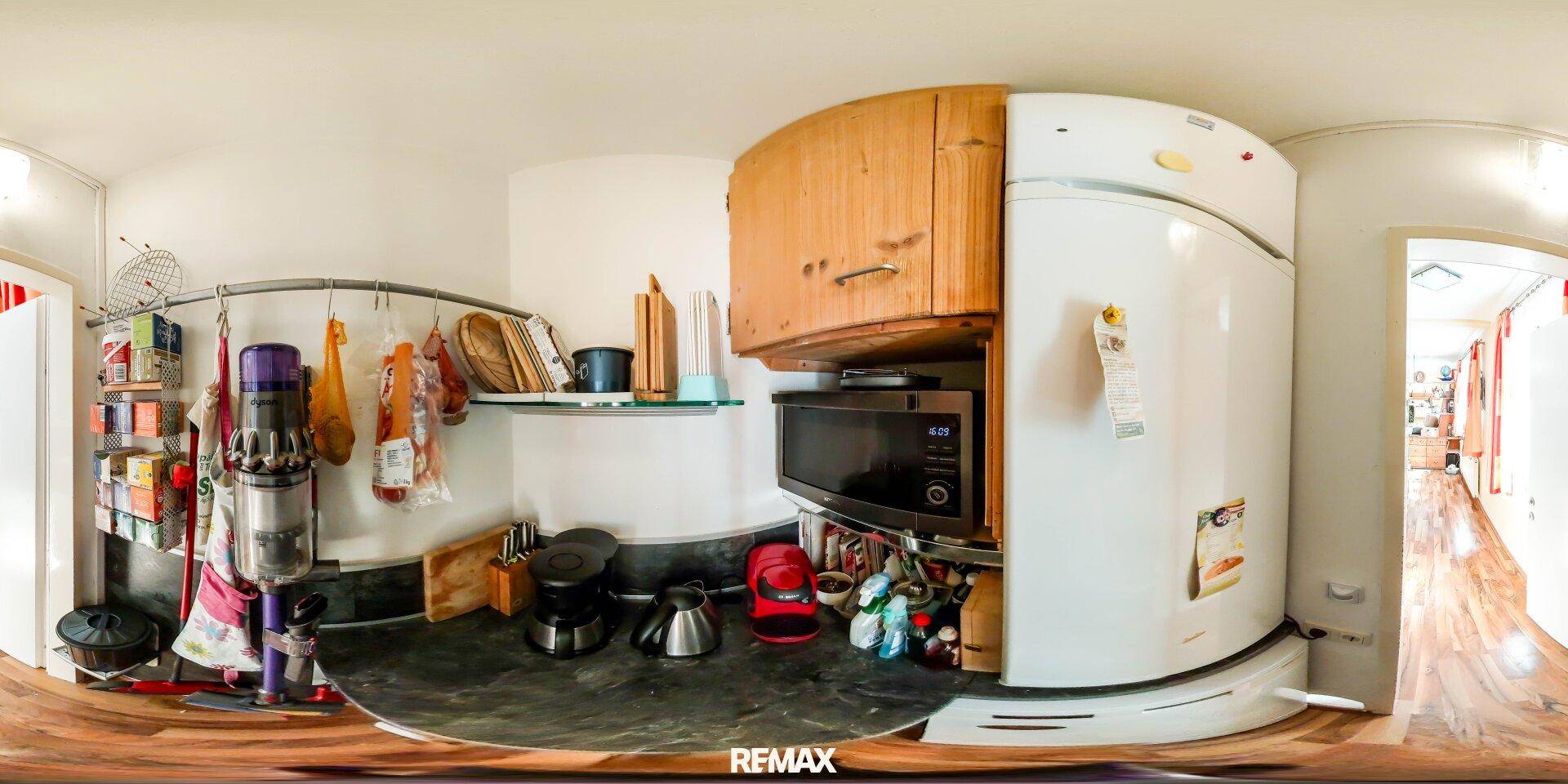 Panoramaansicht einer Küchenecke mit Kühlschrank, Mikrowelle und Stauraum.