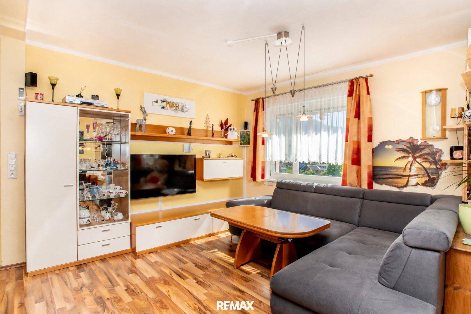Gemütlicher Wohnbereich mit großem Ecksofa, Fernseher und Blick durch das Fenster.