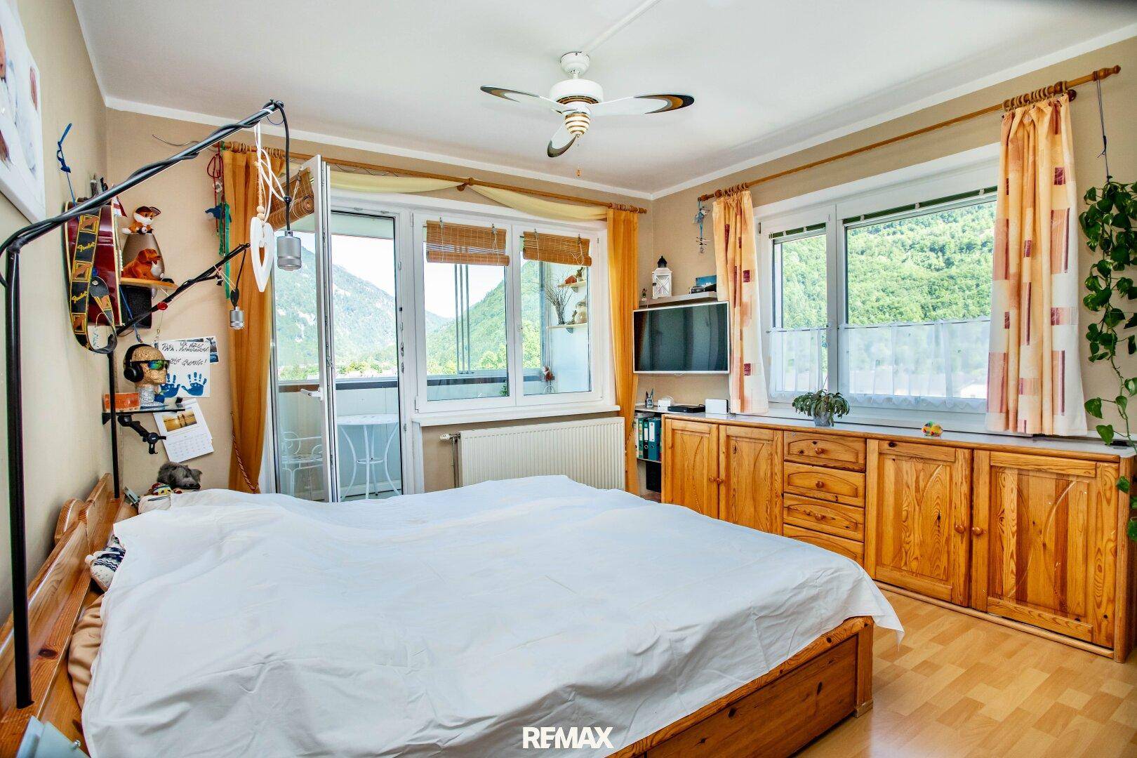 Helles Schlafzimmer mit Holzbett, Deckenventilator und direktem Zugang zum Balkon mit Bergblick.